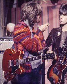 two men standing next to each other holding guitars