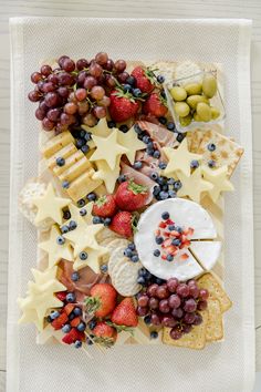 cheese, fruit and crackers are arranged on a white napkin with stars around them