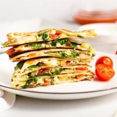 a stack of quesadillas sitting on top of a white plate next to a tomato