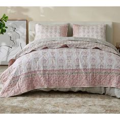 a bed with pink and white bedspread on top of it next to a potted plant