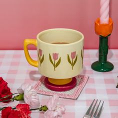 a coffee cup sitting on top of a table next to flowers and a candle holder