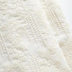 an embroidered white fabric with small flowers and leaves on the side, as well as beads