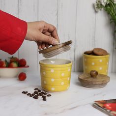 a person pouring coffee into a yellow cup with white polka dots on it and strawberries in the background