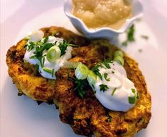 two crab cakes with sour cream and green onions on a white plate next to a dipping sauce