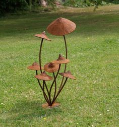 a metal sculpture in the shape of three mushrooms on top of green grass with trees behind it