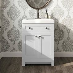 a white sink sitting under a mirror next to a wallpapered wall with a circular mirror