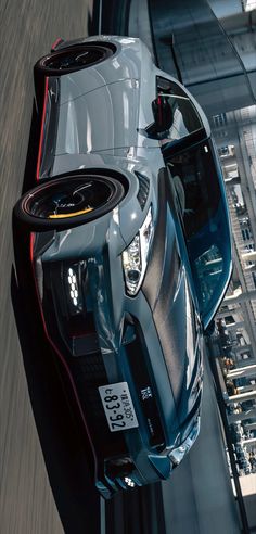 the rear end of a silver sports car driving down a road with buildings in the background