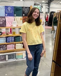 a woman standing in front of a display of t - shirts and other items at a store