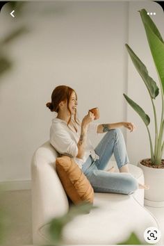 a woman sitting on top of a white couch next to a potted plant