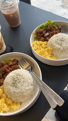 two plates of food with rice, meat and vegetables next to drinks on a table