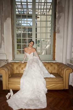 a woman in a white wedding dress sitting on a brown leather couch next to a window