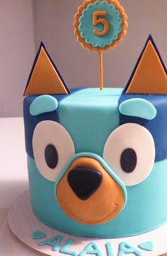 a blue and orange birthday cake with an animal face on it's top tier