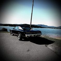 a black car parked on the side of a road next to a body of water