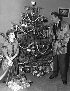 a man and woman standing in front of a christmas tree with presents on the floor