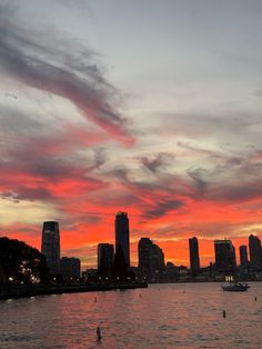 the sky is red and orange as the sun sets over some buildings on the water