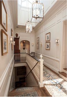 a hallway with stairs and pictures on the wall next to each other in front of a chandelier