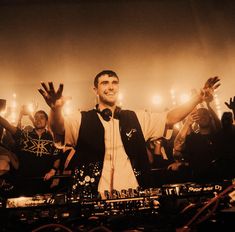 a man standing in front of a crowd holding his hands up and wearing headphones