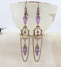 a pair of earrings with dangling chains and purple beads on a white plate next to a bowl