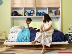 a woman sitting on top of a bed next to a little boy in a room