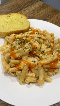 a white plate topped with pasta covered in sauce next to a slice of bread on top of a wooden table