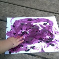 a child's hand is touching a piece of paper with purple paint on it