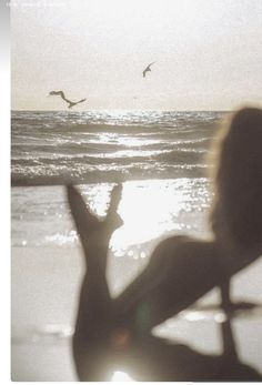 a woman standing on top of a beach next to the ocean with birds flying overhead