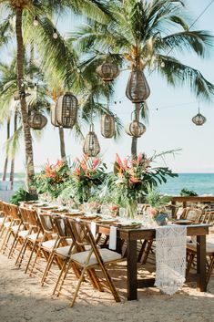 a table set up on the beach for an outdoor wedding reception with hanging lanterns and tropical flowers