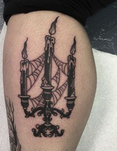 a black and white photo of a candle holder tattoo on the thigh, with two candles in it