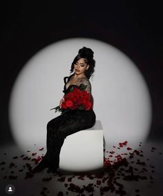 a woman sitting on top of a white box with roses in her lap and red petals around her