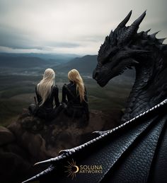 two women sitting on top of a rock next to a dragon