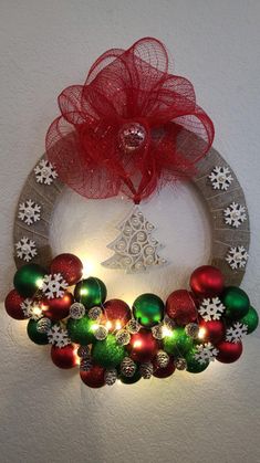 a wreath with christmas ornaments and lights on the front is hung on a wall by a red bow