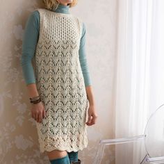 a woman standing in front of a window wearing boots and a crocheted dress