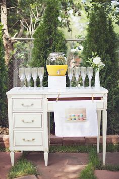 a table with wine glasses and vases on it, next to a lemonade stand