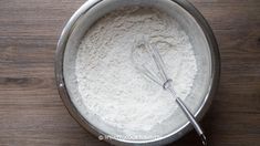 a metal bowl filled with flour and whisk on top of a wooden table