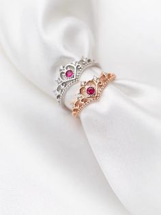 two rings are sitting on top of a white cloth with pink stones in the middle