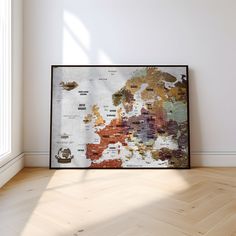 a framed map is sitting on the floor in an empty room with white walls and wooden floors