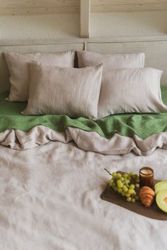 a bed with two pillows and some fruit on top of it next to a tray of grapes