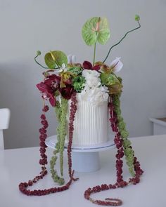 a white cake decorated with flowers and greenery on a table next to a necklace