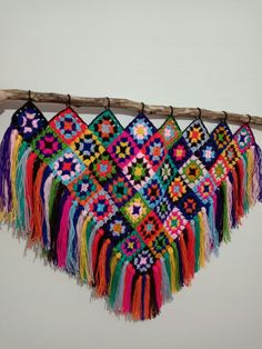 a multicolored crocheted blanket hanging from a wooden stick on the wall