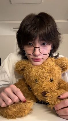 a boy wearing glasses holding a teddy bear in front of his face and looking at the camera