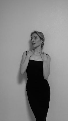 a woman in a black dress is posing for the camera with her hands on her chest