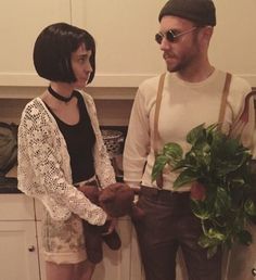 a man standing next to a woman in a kitchen holding a potted plant on the counter