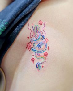 a woman's chest with a colorful dragon tattoo on her left side ribcage