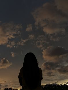 the silhouette of a woman sitting in front of a cloudy sky