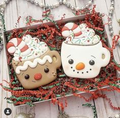 two decorated cookies sitting in a box on top of a wooden table next to christmas decorations