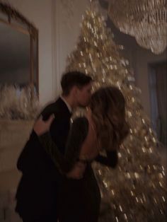 a man and woman kissing in front of a christmas tree with lights on the wall