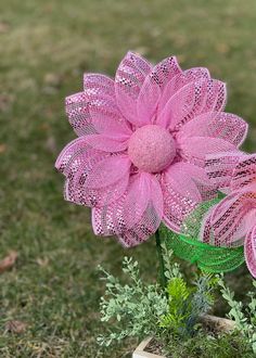 two pink flowers are in a green vase on the grass, and one is made out of mesh