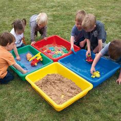 five children playing with toys in their play trays on the grass at a park