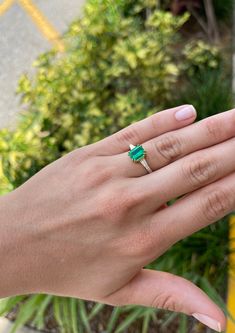 a woman's hand holding an emerald and diamond ring