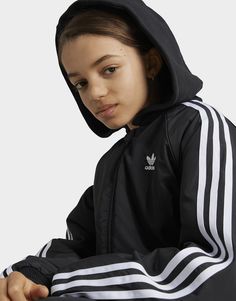 This juniors' Adicolor bomber jacket provides an instant sporty style upgrade to any outfit. Ribbing on the collar, cuffs and hem, plus a detachable hood, provide extra coverage on chilly days. An embroidered Trefoil logo on the chest and 3-Stripes down the sleeves show your connection to adidas' legacy of originality and authenticity. This product is made with 100% recycled materials. By reusing materials that have already been created, adidas help to reduce waste and our reliance on finite resources and reduce the footprint of the products adidas make.• This model is 156 cm and wears a size 11-12Y. Their chest measures 70 cm and the waist 60 cm.• Regular fit• Full zip with ribbed bomber collar• 100% polyester (recycled)• Snap-button side pockets• Ribbed cuffs and hem• Detachable hood Adidas Adicolor, Adidas Kids, Style Upgrade, Reduce Waste, Jd Sports, Detachable Hood, Sporty Style, Black Adidas, Kids Jacket